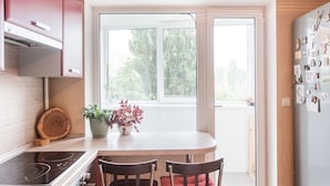A kitchen with a dining table, chairs, a stove, and a window with a view of trees. - MalinaApt Sea Place (Kyiv)