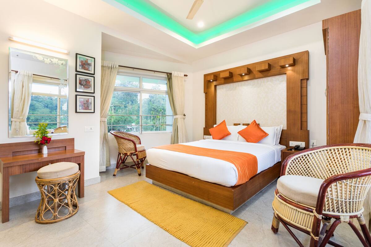 A bedroom with a large bed, a wooden headboard, a desk, a chair, and a window with curtains.