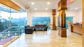 Eine großzügige Lobby mit einer Rezeption, einer Sitzecke und einer Glaswand mit Blick ins Freie.