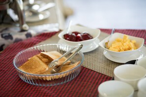 A breakfast setting with toast, fruit, and a glass bowl on a checkered tablecloth. - Monsoon Grande (Devikolam)