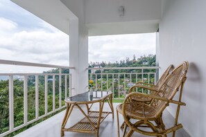 A balcony with wicker furniture and a glass table, overlooking a lush green landscape. - Monsoon Grande (Devikolam)