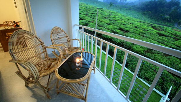 Ein Balkon mit Korbstühlen und einem Tisch, mit Blick auf eine üppige, grüne Teeplantage.
