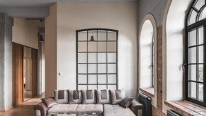A modern living room with a sectional sofa, a glass coffee table, and large windows with arched designs. - Aparthotel Stara Przędzalnia (Żyrardów)