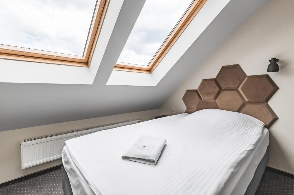 A hotel room with a skylight, a bed with a neatly folded towel, a radiator, and a hexagonal wall panel.