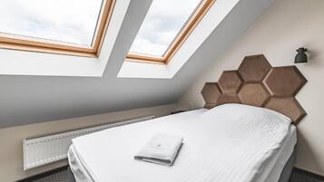 A hotel room with a skylight, a bed with a neatly folded towel, a radiator, and a hexagonal wall panel.