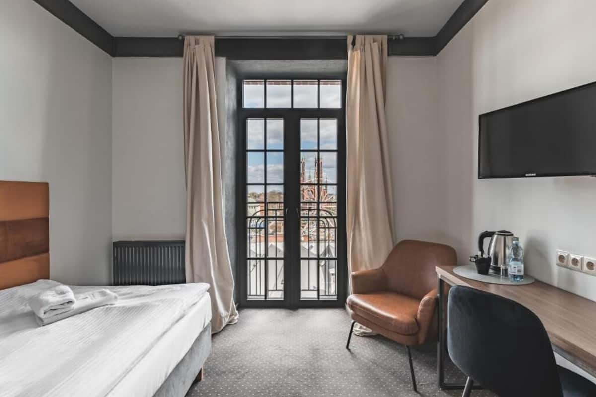 Habitación de hotel con cama, escritorio, silla, televisor y ventana con cortinas.