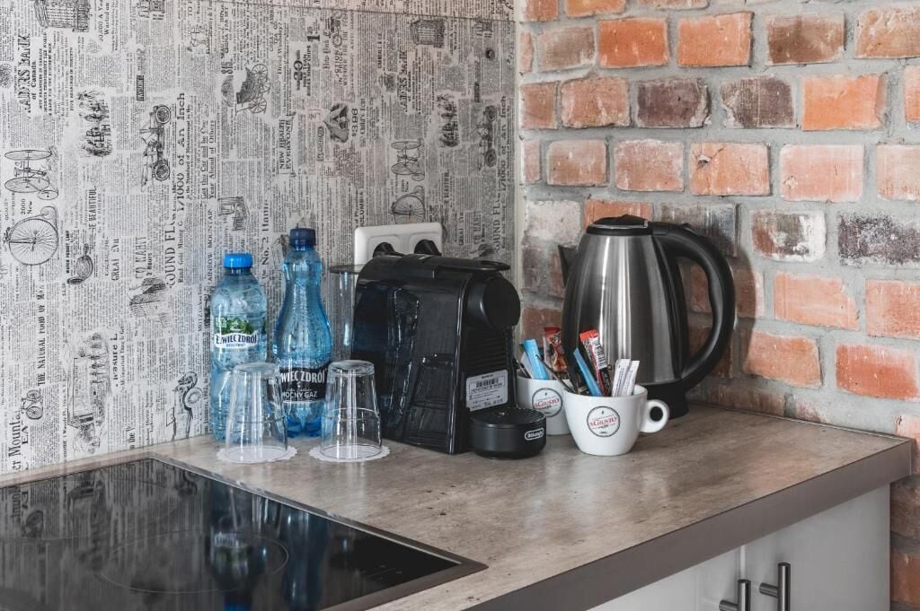 Uma bancada de cozinha com um revestimento de parede estampado com jornal, uma cafeteira, um bule e uma caneca com utensílios.