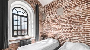 A room with a brick wall, a window with a view, a bed, and a small table. - Aparthotel Stara Przędzalnia (Żyrardów)