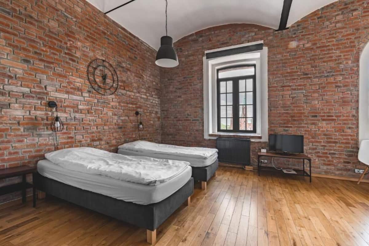 Una habitación con dos camas, una pared de ladrillo, una ventana y un televisor.