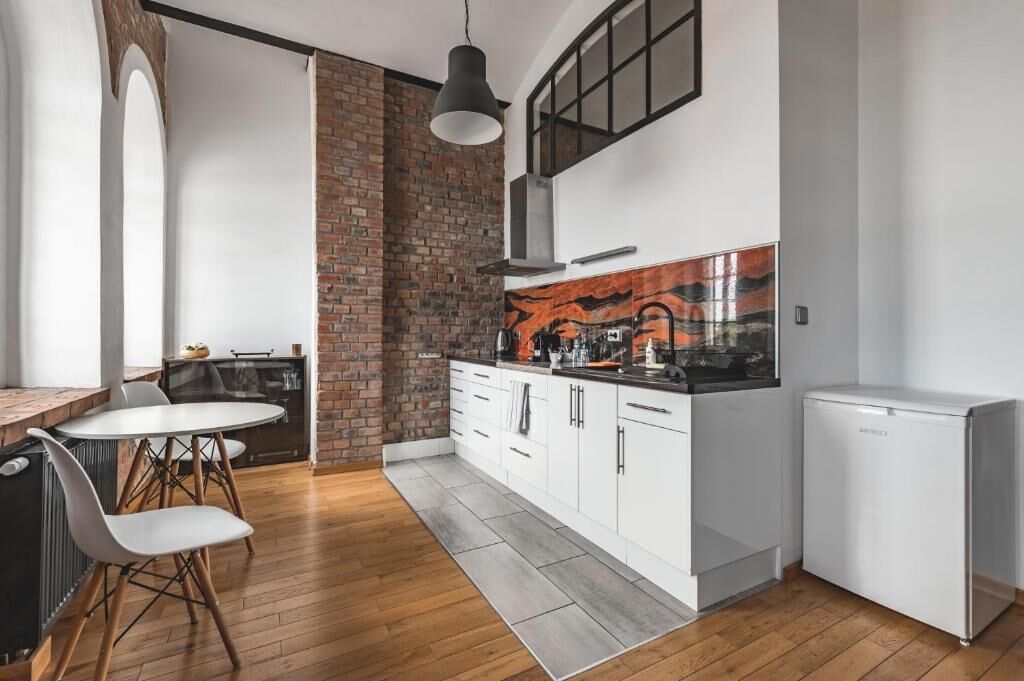 Una cocina compacta con armarios blancos, una pared de ladrillo decorativa y una lámpara colgante moderna.