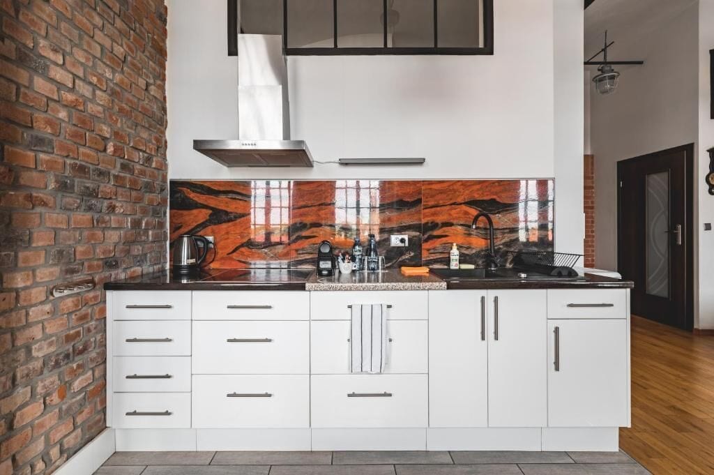 A modern kitchen with white cabinets, a black countertop, and a red marble backsplash.