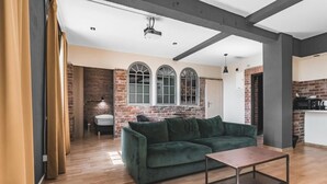 A modern living room with a green sofa, a wooden coffee table, and a brick wall with arched windows. - Aparthotel Stara Przędzalnia (Żyrardów)