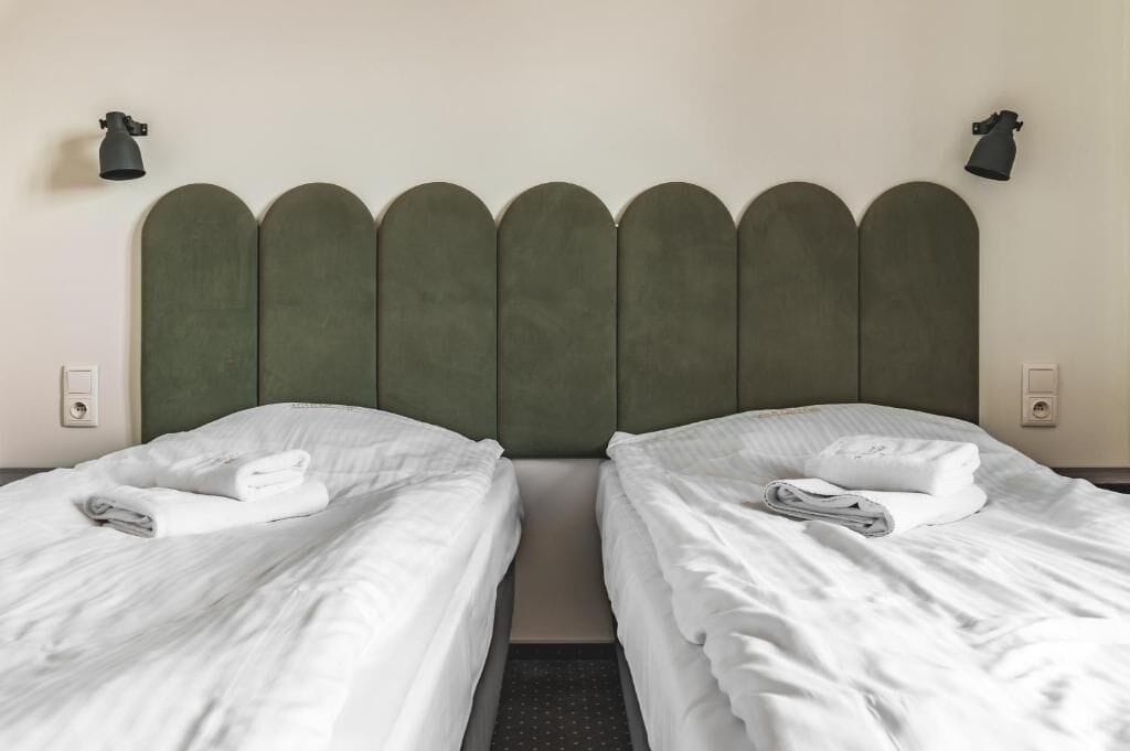 Habitación de hotel con dos camas, cada una con toallas blancas ordenadas.