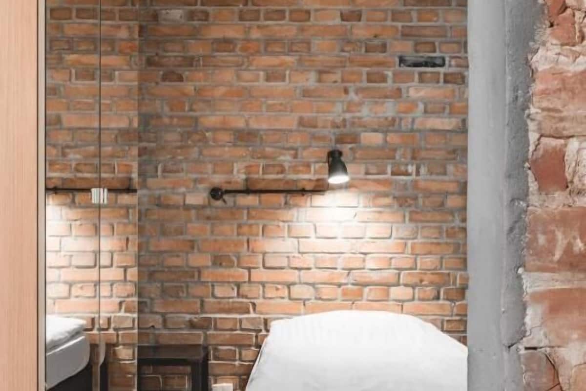 Un dormitorio con pared de ladrillo, cama, mesita de noche y espejo.