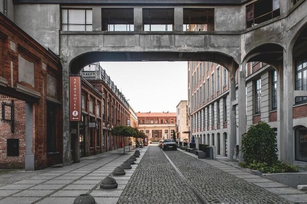 A cobblestone street under an archway with buildings on either side, including a sign for "APARTHOF FI". - Aparthotel Stara Przędzalnia (Żyrardów)