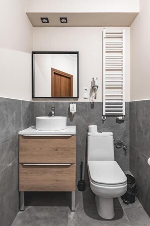A modern bathroom with a white sink, wooden vanity, a toilet, and a towel rack. - Aparthotel Stara Przędzalnia (Żyrardów)