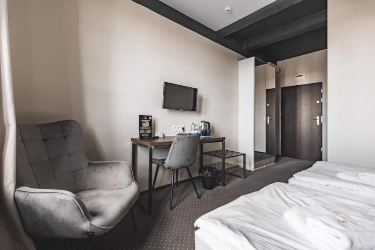 Una habitación de hotel con cama, escritorio, silla, televisor y puerta de baño.