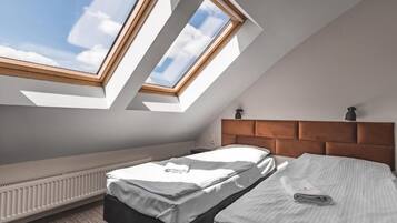 Camera da letto con soffitto a falde, lucernari, un letto, un comodino e un termosifone.