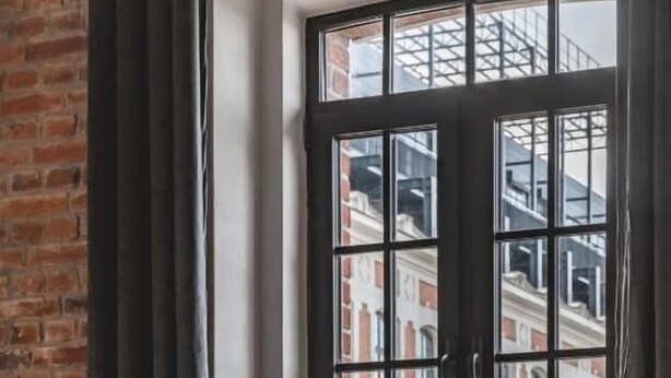 A room with a large window, a brick wall, and two dark chairs. - Aparthotel Stara Przędzalnia (Żyrardów)