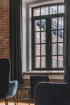 Ein Zimmer mit großem Fenster, einer Backsteinwand und zwei dunklen Stühlen.