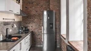 A modern kitchen with a brick wall, stainless steel appliances, and a window with an arched design. - Aparthotel Stara Przędzalnia (Żyrardów)