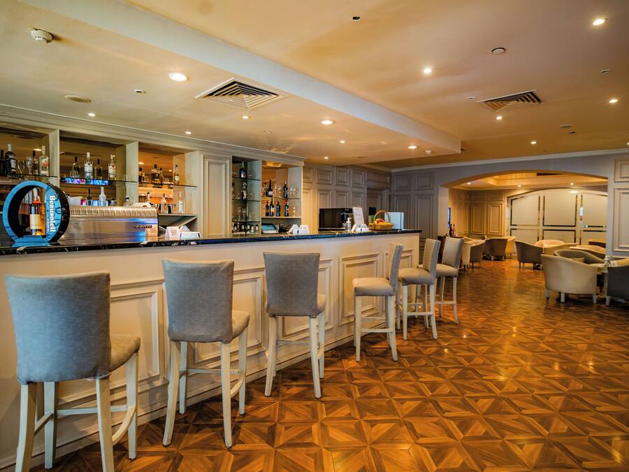 A bar area with a polished wooden floor, bar stools, and a well-stocked bar counter.