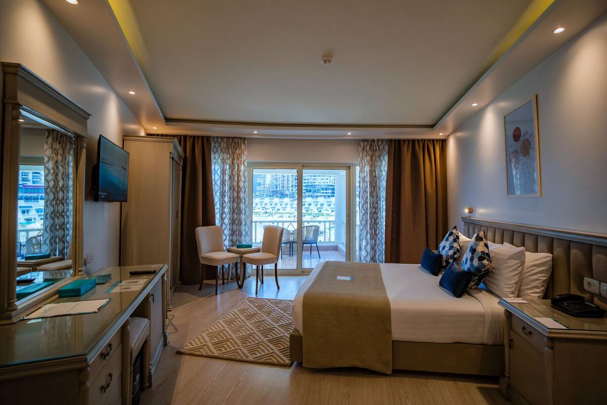 Une chambre d’hôtel avec un lit, un bureau, une chaise et une vue sur la ville par la fenêtre.