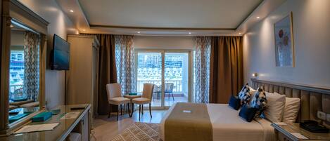 Quarto de hotel com cama, escrivaninha, cadeira e vista da cidade pela janela.