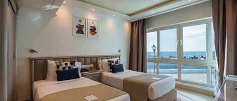 A hotel room with two beds, a large window with a view of the sea, and a ceiling with recessed lighting.