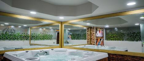 A modern spa area with a large hot tub, wooden paneling, and a mirrored wall reflecting the space.