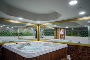 A modern spa area with a large hot tub, wooden paneling, and a mirrored wall reflecting the space. - SUNRISE Alex Avenue Hotel (Alexandria)