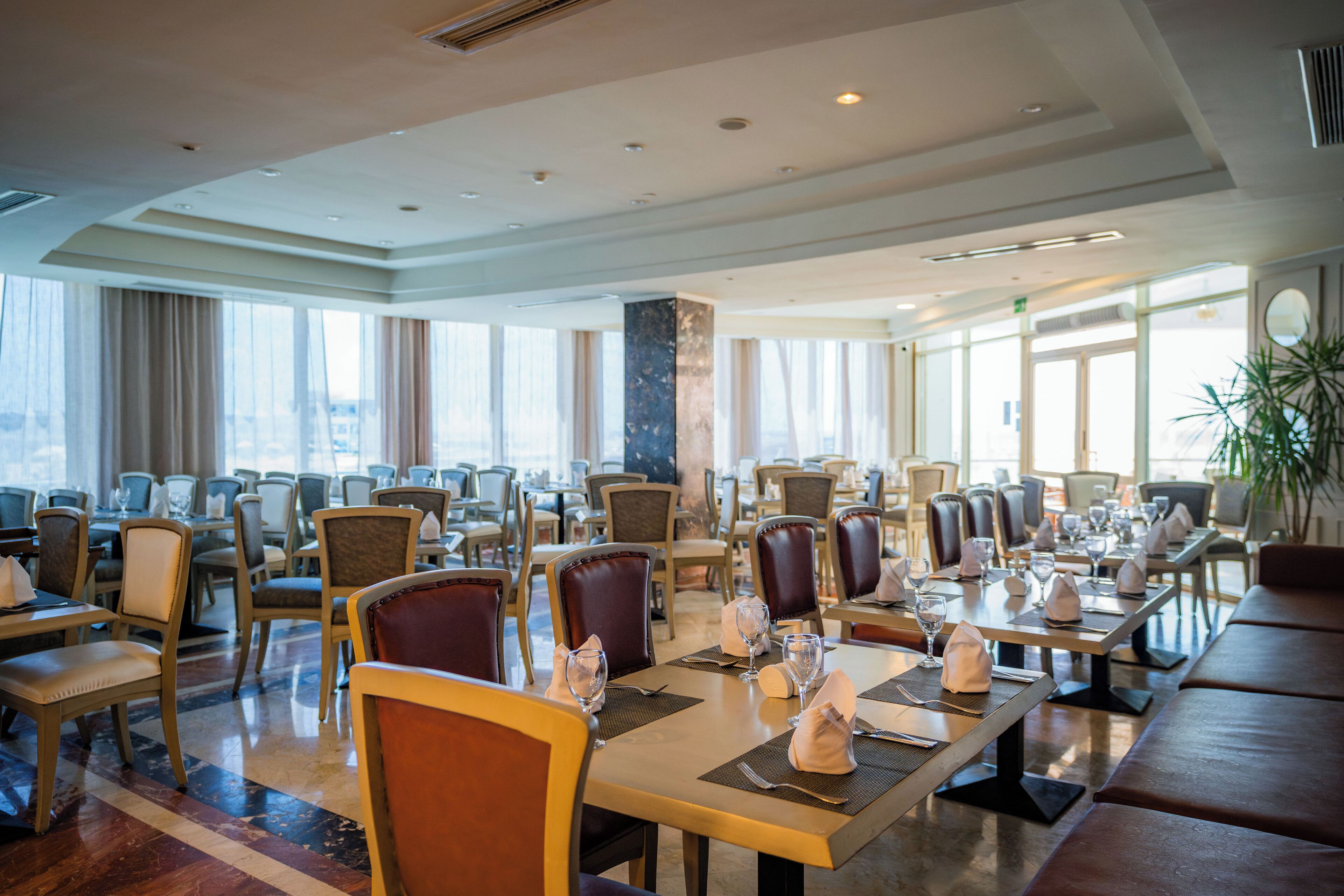 A spacious dining area with multiple tables and chairs, large windows, and a modern interior design.