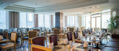 A spacious dining area with multiple tables and chairs, large windows, and a modern interior design.