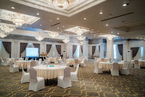 A conference room with round tables, white chairs, chandeliers, and a projection screen. - SUNRISE Alex Avenue Hotel (Alexandria)