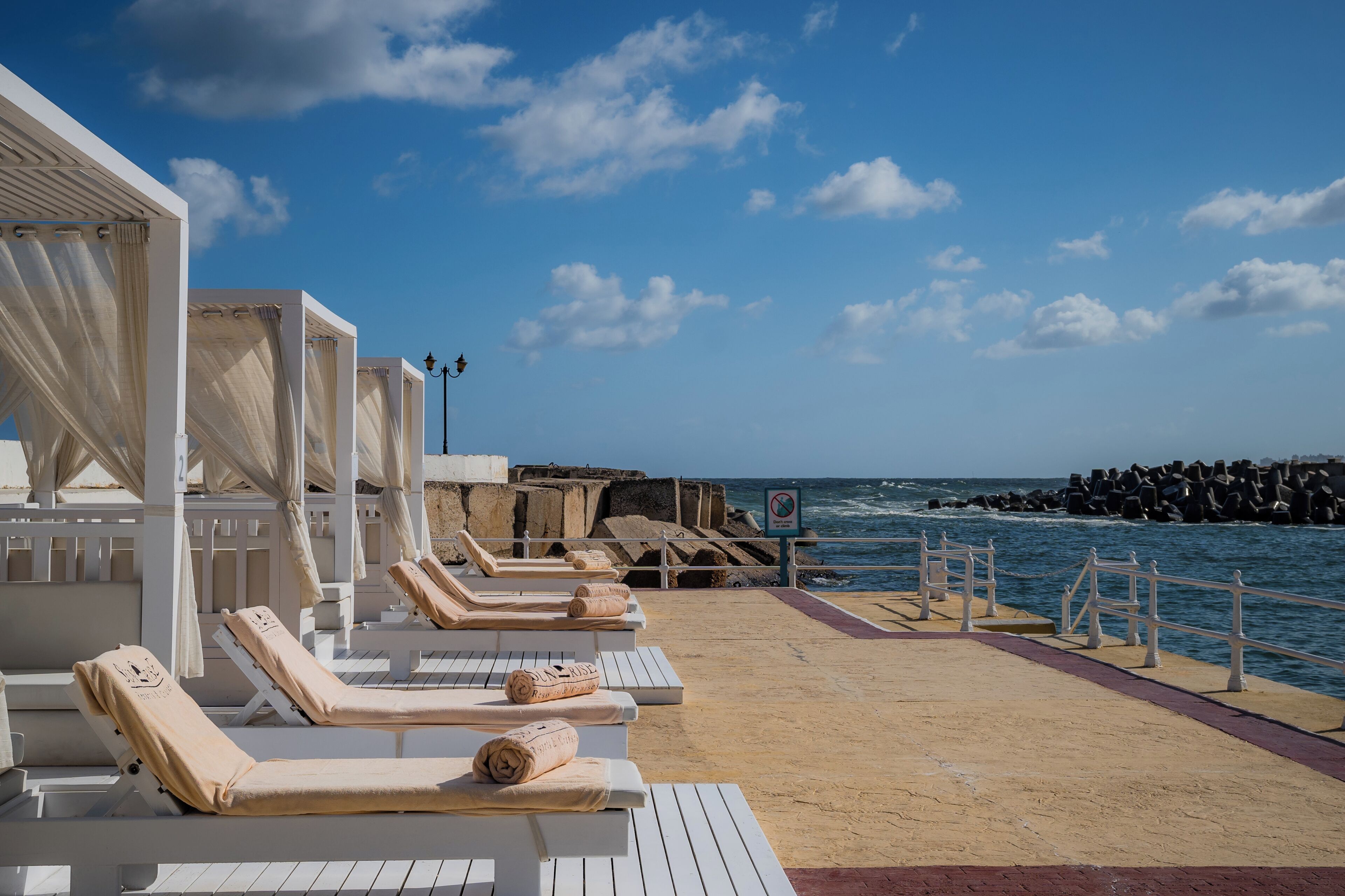Zona relax in spiaggia con lettini bianchi, una zona salotto coperta e vista sul mare.
