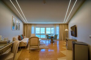 A modern hotel room with a sofa, chairs, a dining table, a TV, and a view of the cityscape. - SUNRISE Alex Avenue Hotel (Alexandria)