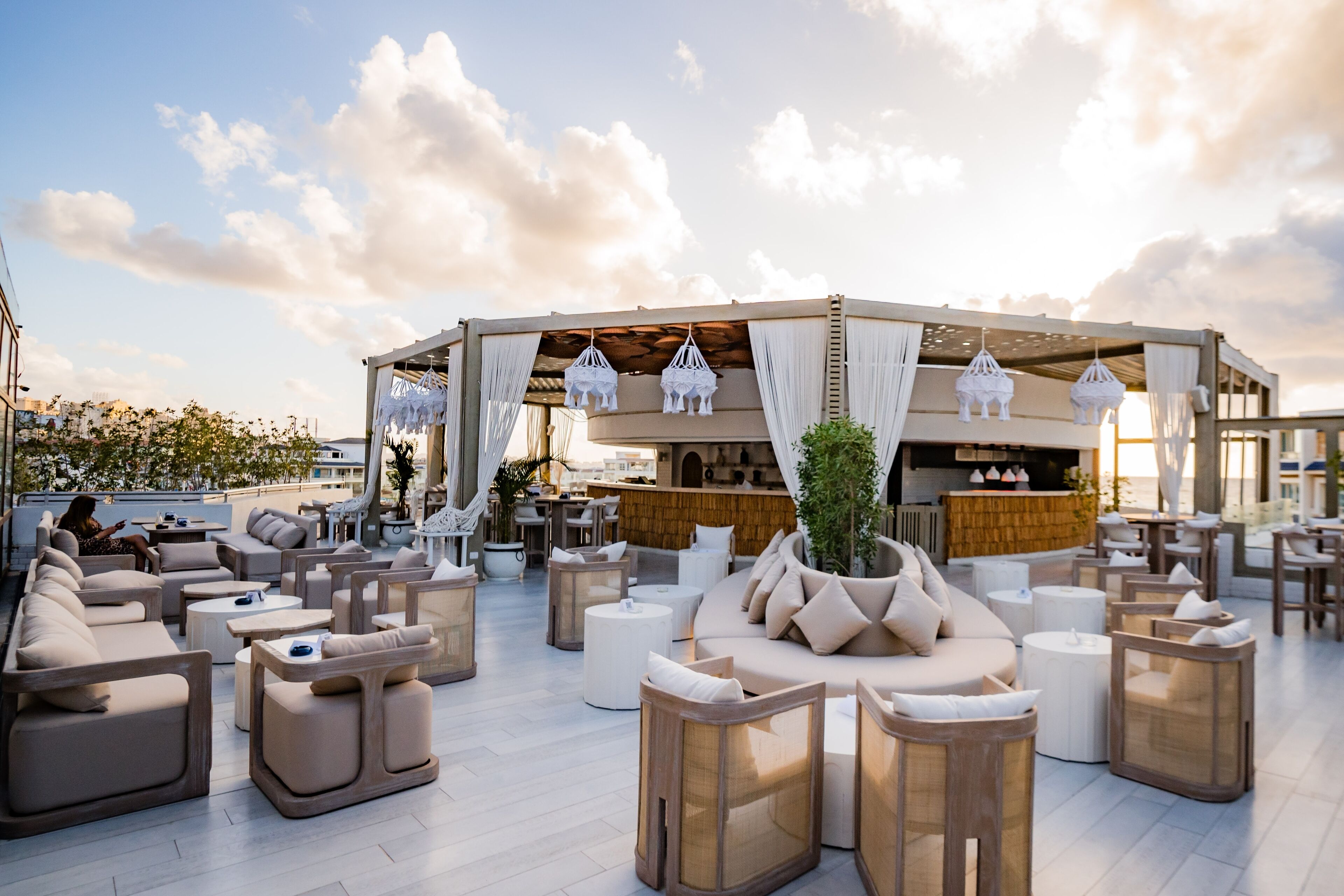 Eine Dachterrasse mit Sitzgelegenheiten im Freien, einer Bar und Blick auf die Skyline der Stadt.