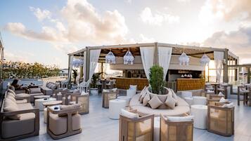 Eine Dachterrasse mit Sitzgelegenheiten im Freien, einer Bar und Blick auf die Skyline der Stadt.