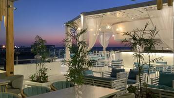 An outdoor seating area with tables and chairs, a pergola structure, and potted plants.