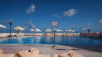 Un espace aménagé au bord de la piscine, avec des chaises longues, des parasols et un panneau indiquant qu’il est interdit de se baigner ou de plonger.