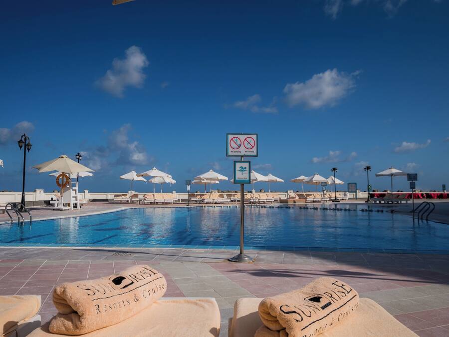Un espace aménagé au bord de la piscine, avec des chaises longues, des parasols et un panneau indiquant qu’il est interdit de se baigner ou de plonger.