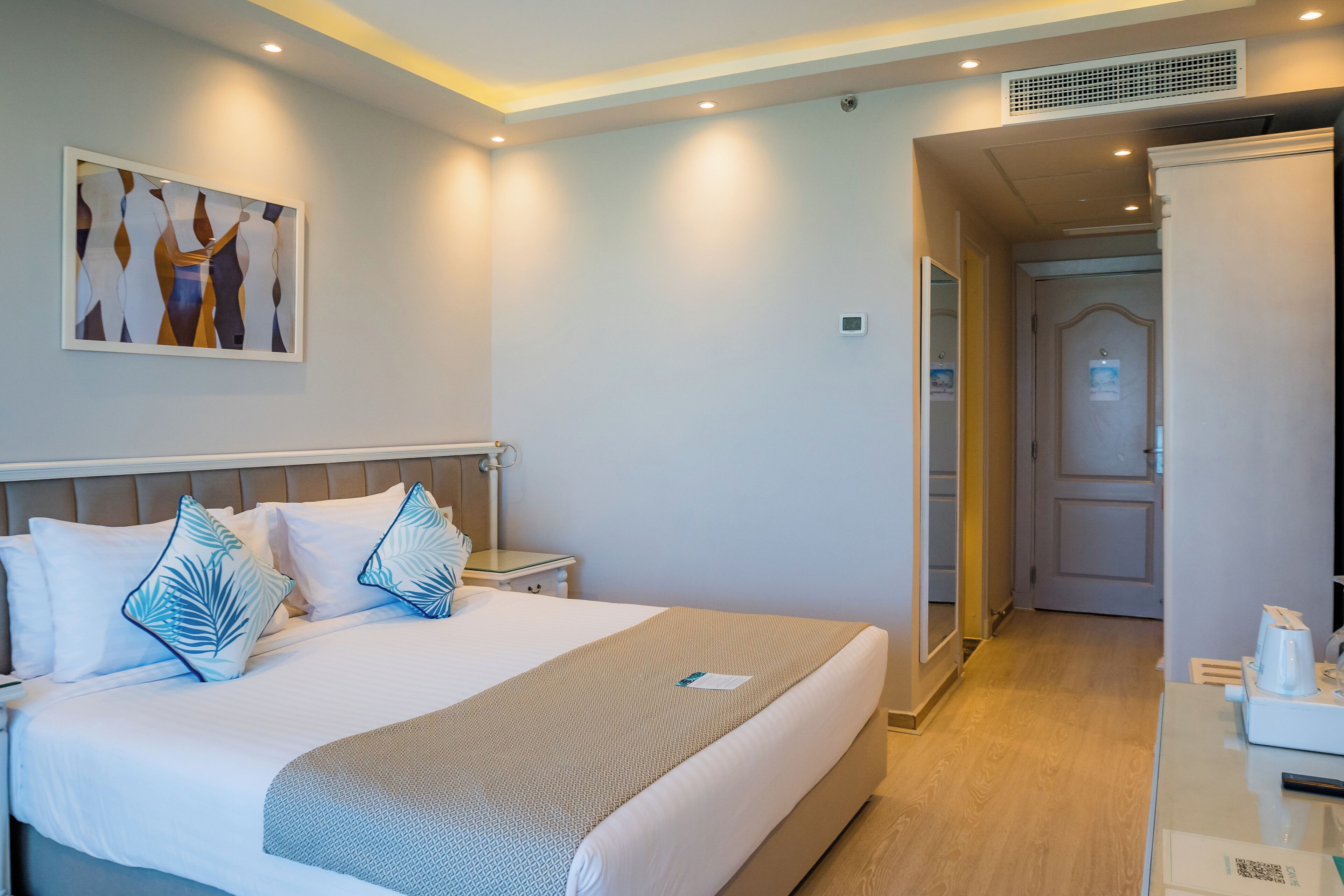 Habitación de hotel con una cama, mesitas de noche, un espejo y una puerta que da a otra habitación.