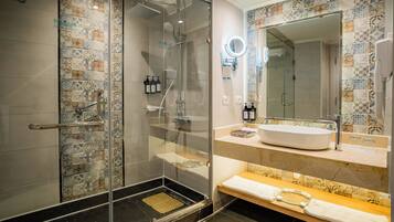 A modern bathroom with a glass-enclosed shower, a sink with a mirror, and patterned tiles.