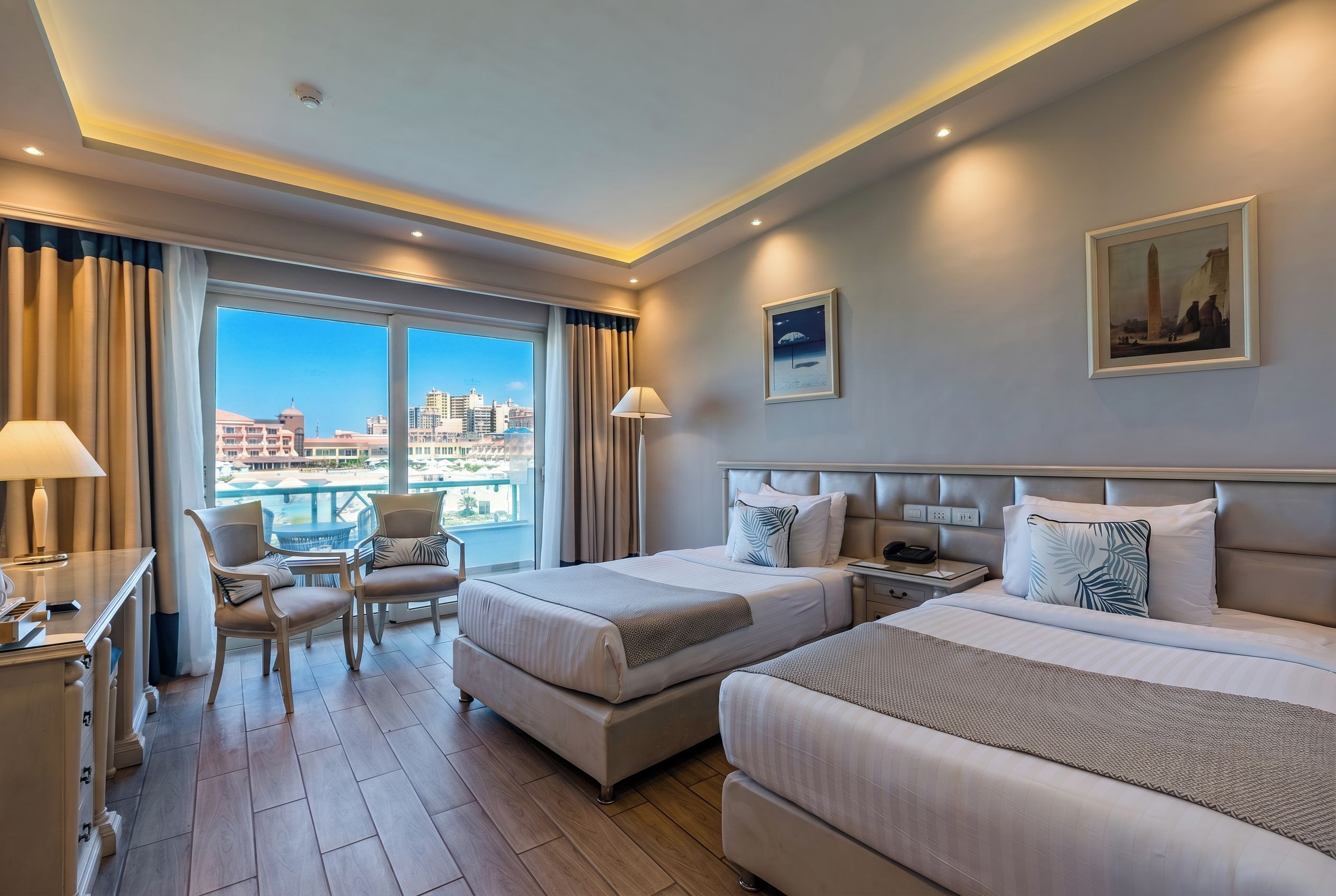 Habitación de hotel con dos camas, un escritorio, una silla y vistas a la ciudad.
