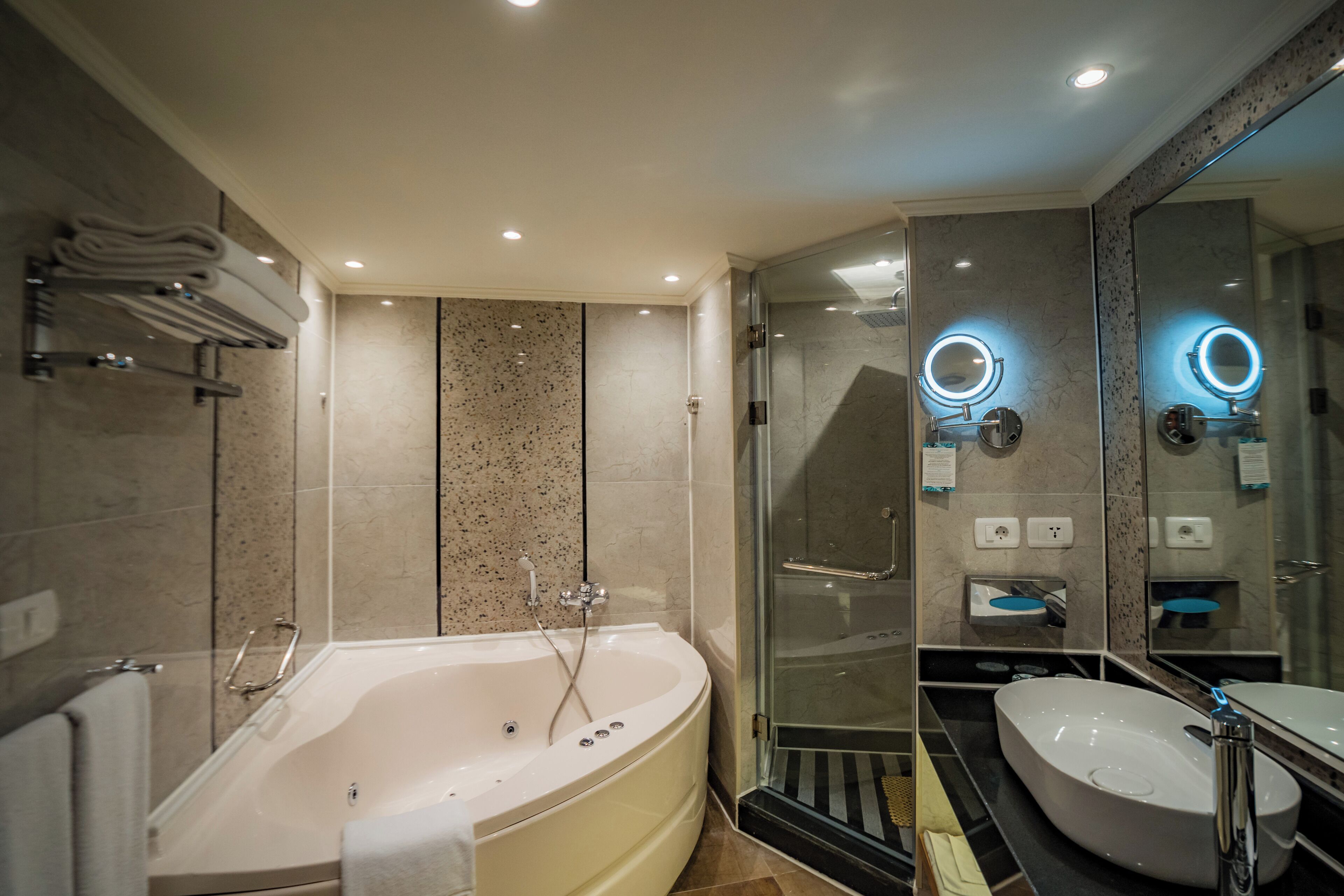 A modern bathroom with a freestanding bathtub, a glass-enclosed shower, and a vanity with a large mirror and under-mirror lights.