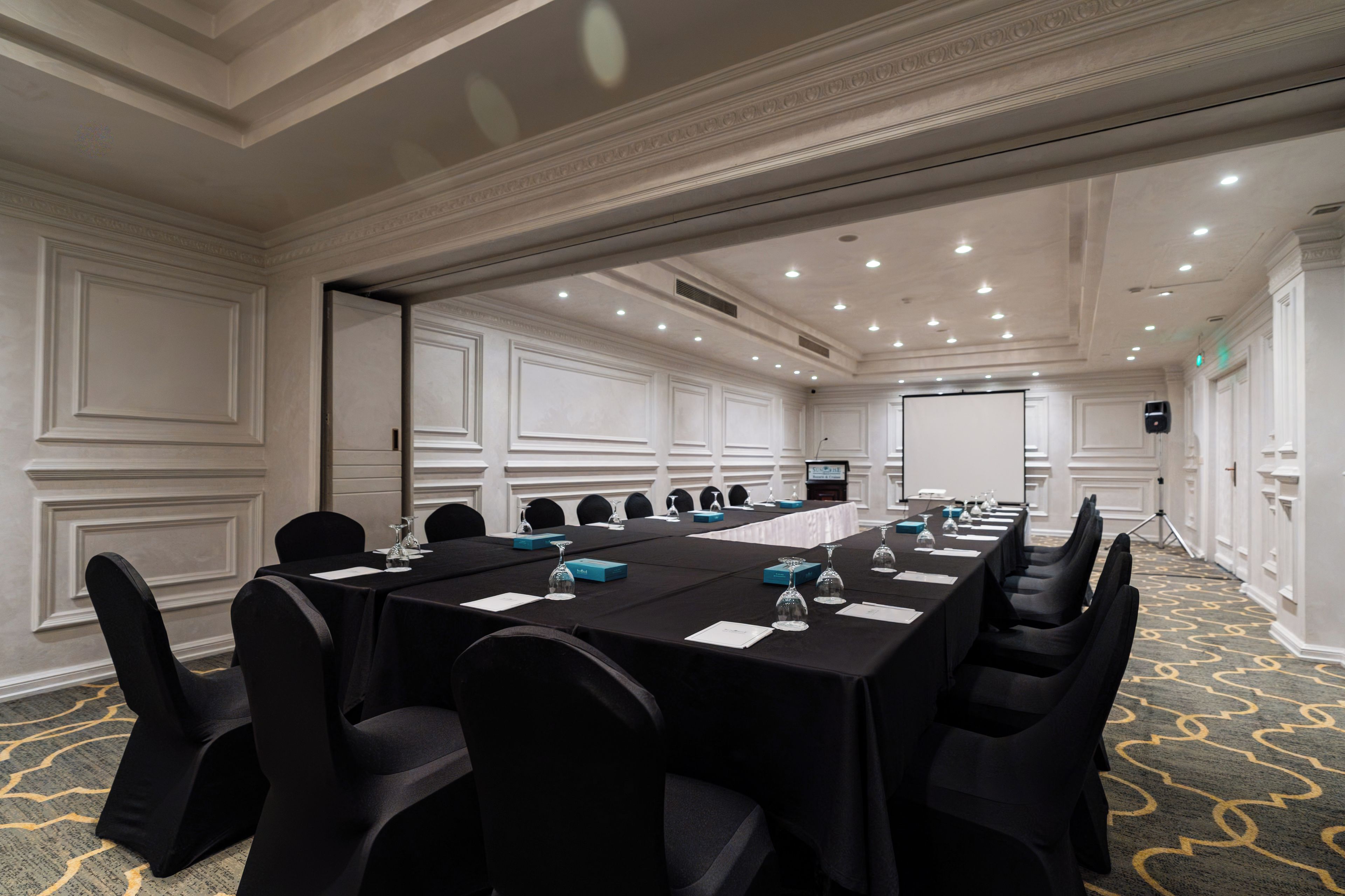 A conference room with a long table, chairs, and a projector screen.