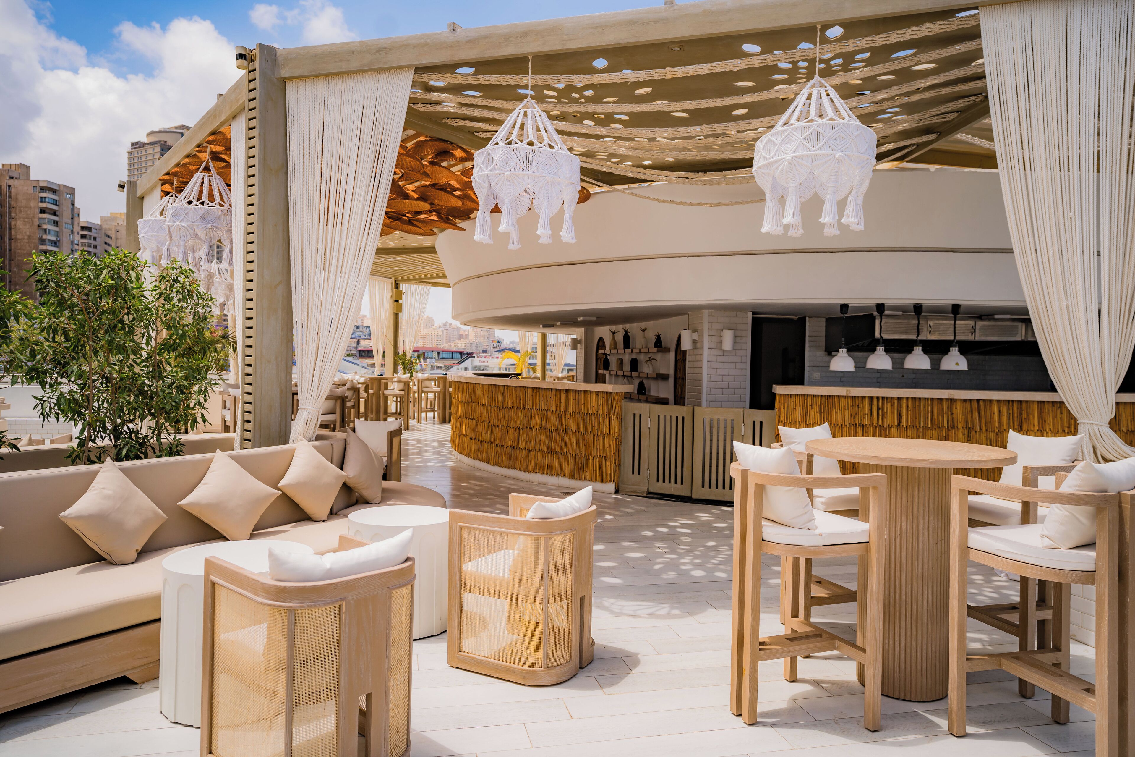 Un área de estar moderna al aire libre con barra, sofás acolchados y sillas de madera.