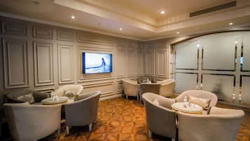 Un amplio salón con una gran televisión de pantalla plana montada en la pared, diversas opciones de asiento que incluyen sillones y sofás, y un suelo de madera con diseño.