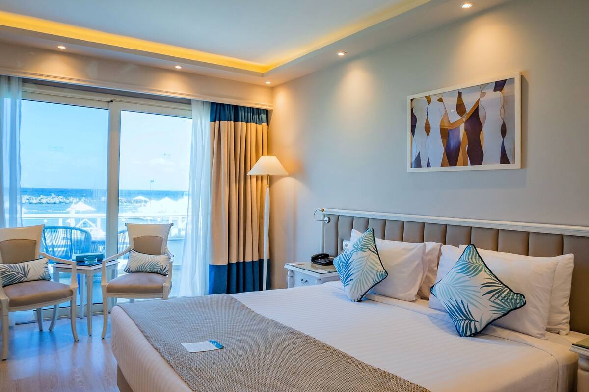 Une chambre d’hôtel avec un lit, deux chaises, une table de chevet, une lampe et un tableau au mur.