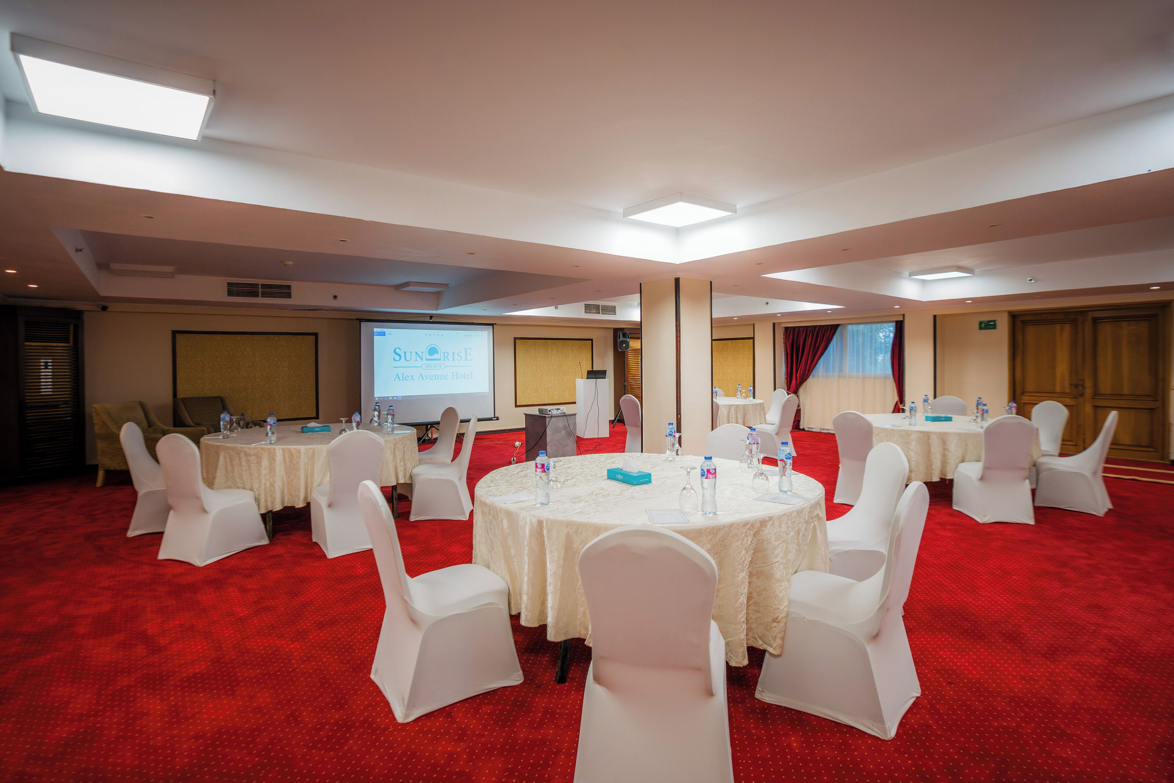 Un salón de conferencias con mesas redondas, sillas blancas y una alfombra roja.